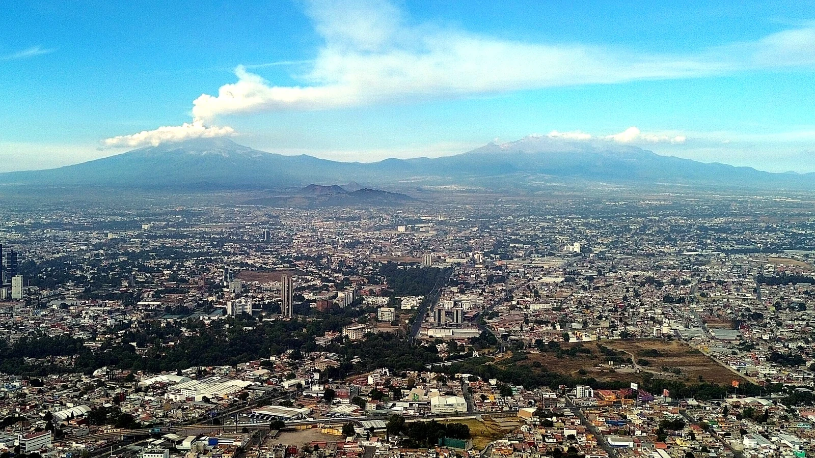 Panorámica real del Popocatépetl, con fumarola, y el Iztaccíhuatl sobre el poniente de Puebla y las torres de Angelópolis